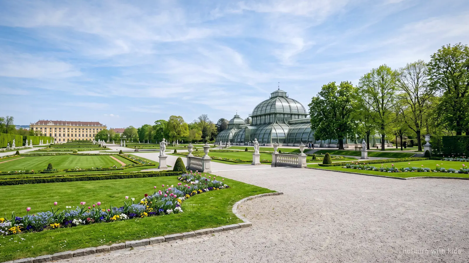 A bright palace garden in Vienna in late spring, with lawns and a glasshouse behind